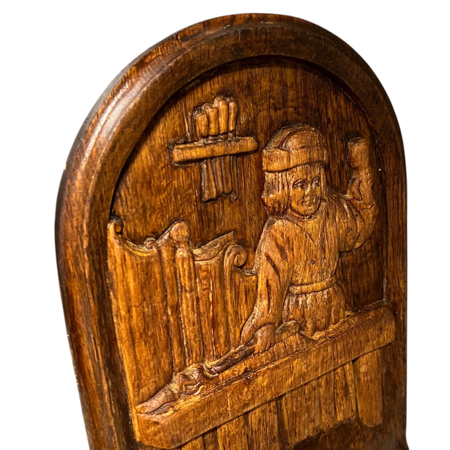 Wooden plaque with a carved scene of a person holding a flute and a shield on a white background
