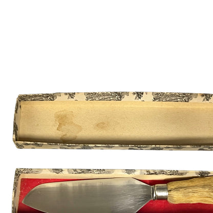A metal cake or pastry server with a taxidermy deer handle resting in a red-lined box, shown with the open patterned box above on a white background.