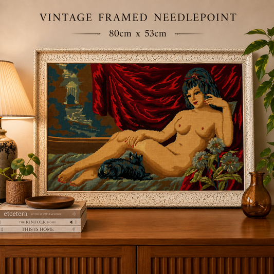 Large French vintage tapestry in a white frame, featuring a reclining nude, perfect for a tapestry collector, set against a countertop beside a lamp with a pile of books and a plant