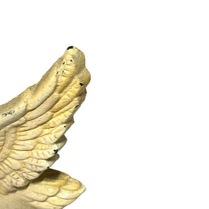 A close-up of a textured, cream-colored winged sculpture or decorative object on a plain white background.