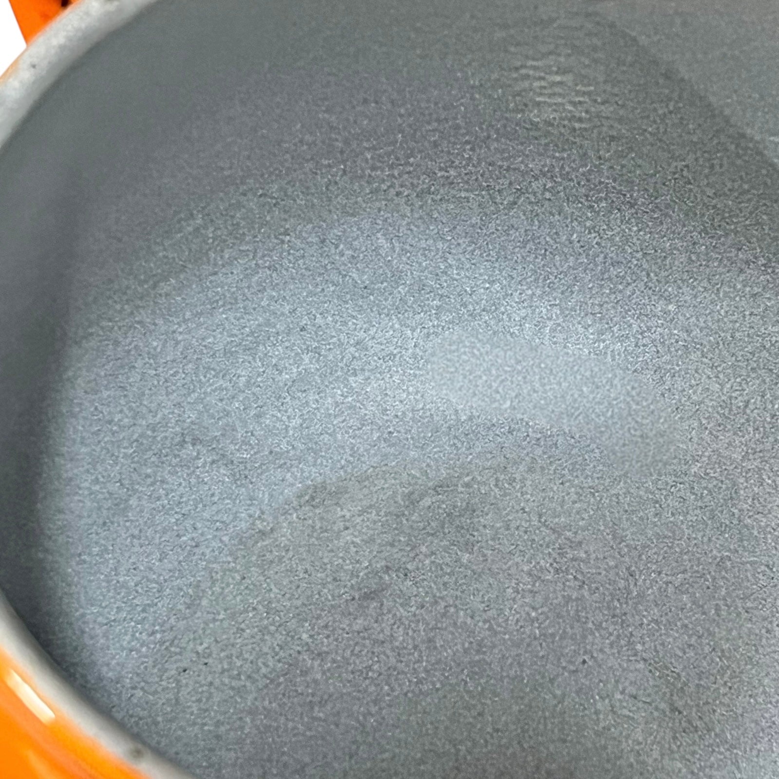 Close-up of the textured grey interior of a pot or pan, showing a speckled enamel-like finish with a sliver of orange exterior visible at the left edge.
