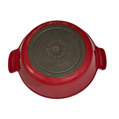 Red enameled cast iron casserole dish shown from the bottom, featuring side handles and a dark gray non-stick coated bottom with embossed 'COUSANGES MADE IN FRANCE' text.