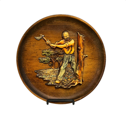 French round vintage wooden wall plaque with a 3d resin/plastic scene in relief of a woodcutter chopping a tree, rustic Arts and Crafts in style, ideal for a country home, set on a white background