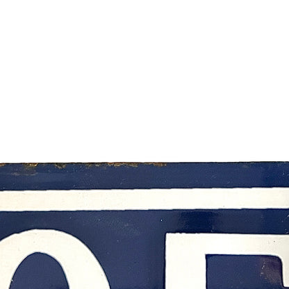 A close-up detail of a dark navy blue painted surface with bold white lettering and a thin white horizontal stripe, showing slight rust or wear along the top edge.