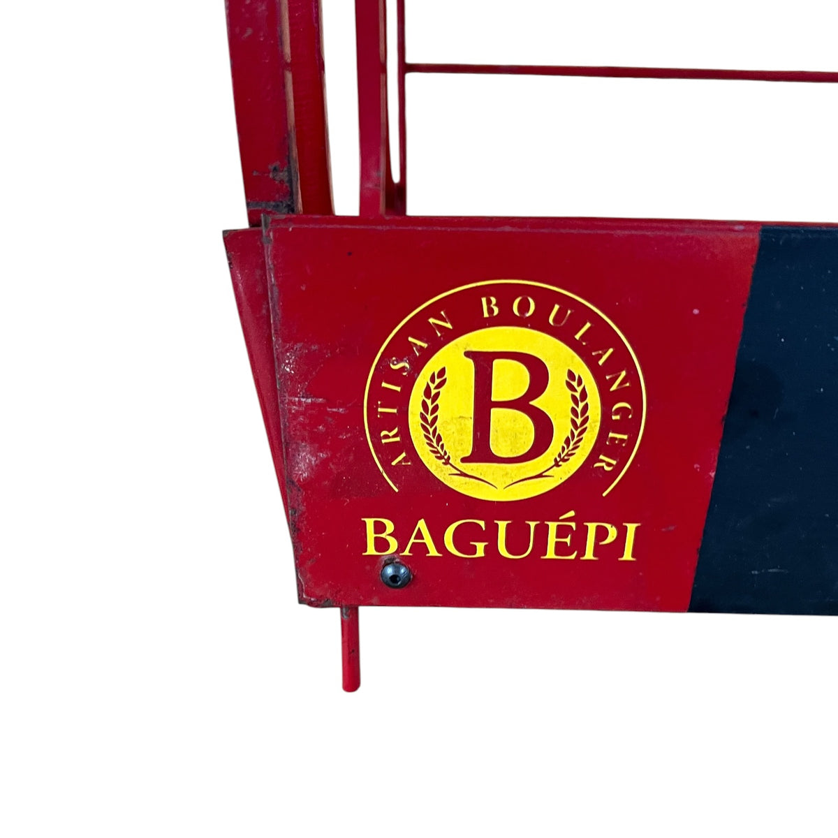 A close-up of a red metal bakery display stand or counter panel with a yellow circular logo reading 'Artisan Boulanger B Baguépi'.