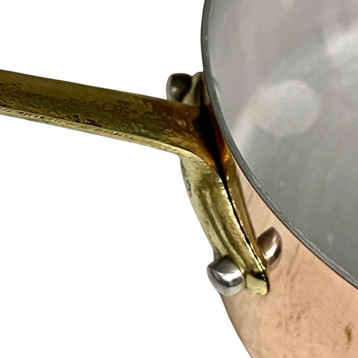 Close-up of a copper pot with a hammered brass handle and silver rivets, set against a plain white background.