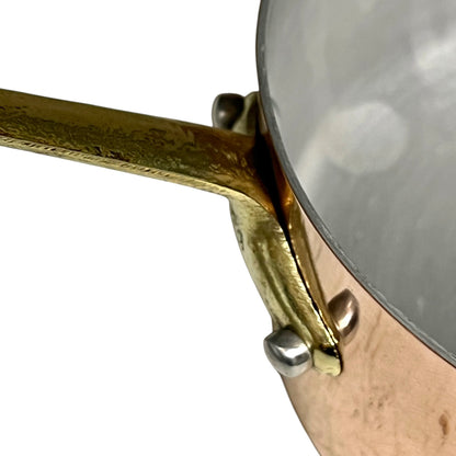 Close-up of a copper pot with a hammered brass handle and silver rivets, set against a plain white background.