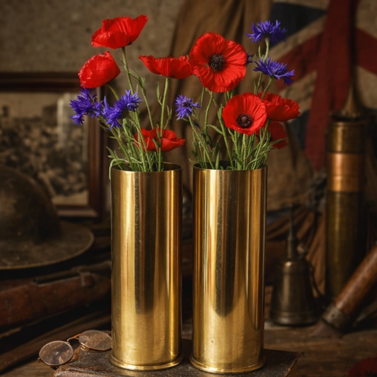 Two brass WW1 shell casings filled with red and blue flowers on a wooden surface.