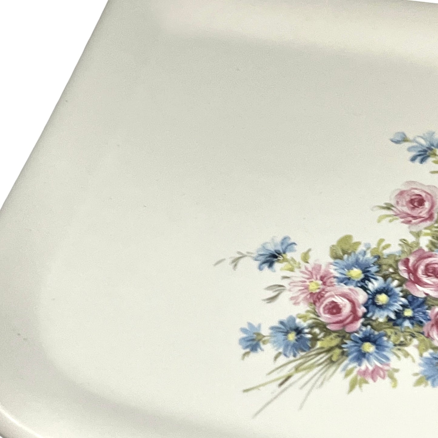 Close-up of a white ceramic shelf with a floral print in the bottom-right corner, featuring pink and blue flowers with green leaves.