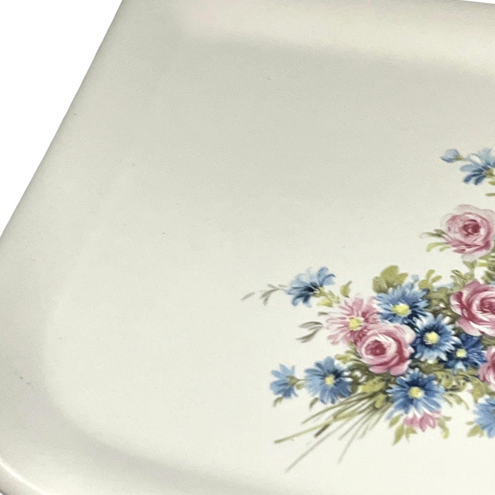 Close-up of a white ceramic shelf with a floral print in the bottom-right corner, featuring pink and blue flowers with green leaves.