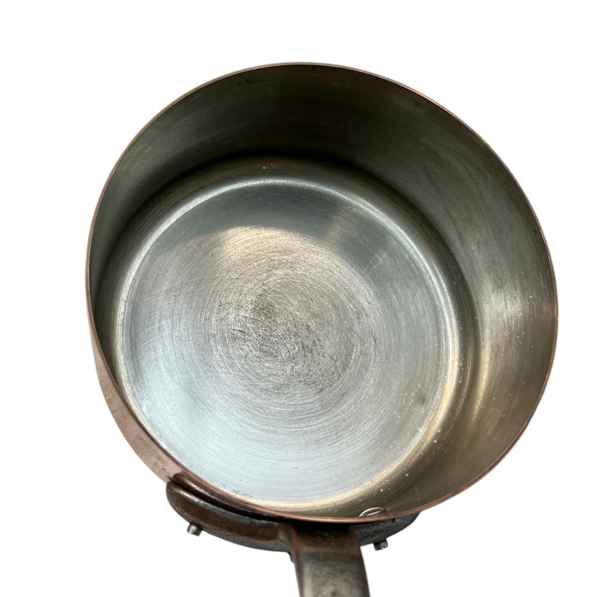 An overhead close-up of a metal saucepan or pot interior with a brushed silver bottom and slightly darker bronze-toned rim, shown on a plain white background.