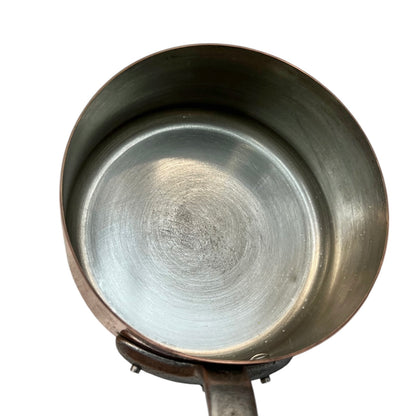 An overhead close-up of a metal saucepan or pot interior with a brushed silver bottom and slightly darker bronze-toned rim, shown on a plain white background.