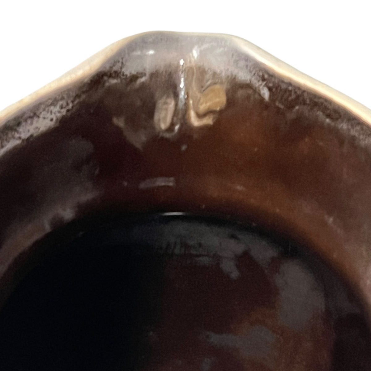 Close-up of the rim of a dark brown glazed ceramic vessel, showing glossy brown and amber tones against a white background.