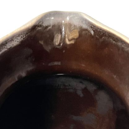 Close-up of the rim of a dark brown glazed ceramic vessel, showing glossy brown and amber tones against a white background.