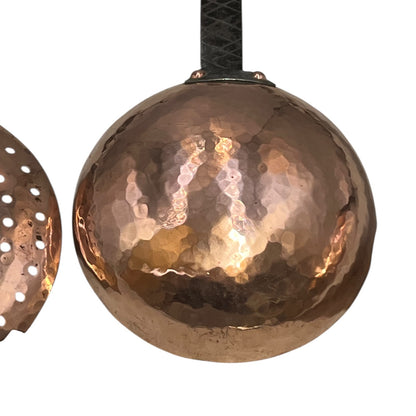 Close up of French copper kitchen utensils with black handles on a white background