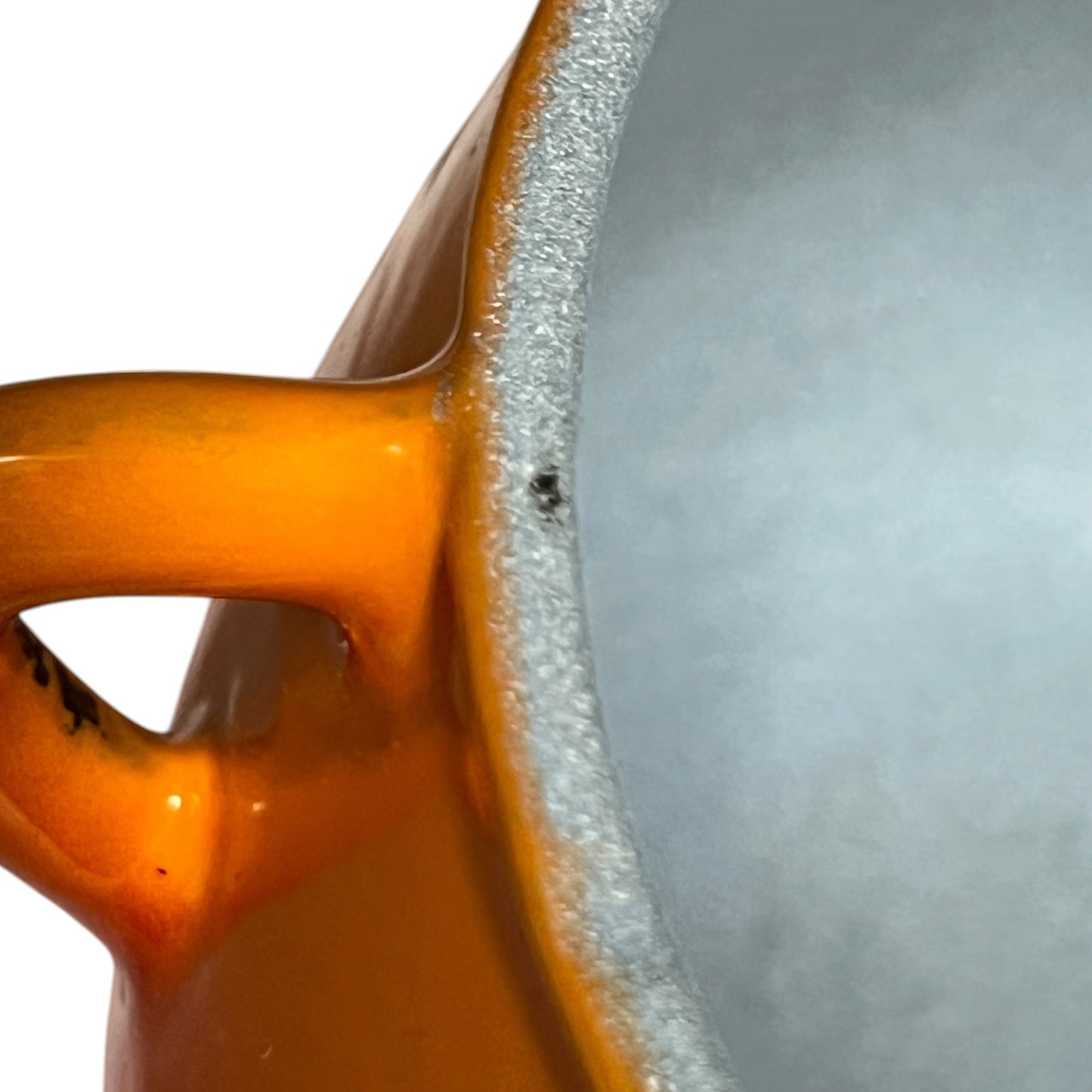 Close-up of an orange ceramic pot showing the glossy glazed exterior handle and the textured light grey interior rim against a white background.