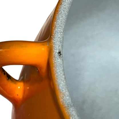 Close-up of an orange ceramic pot showing the glossy glazed exterior handle and the textured light grey interior rim against a white background.