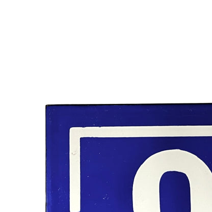 A close-up of a blue and white sign or panel showing part of a white letterform on a blue background, cropped against a white backdrop.