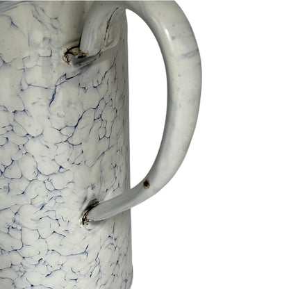 Close up of a vintage-style white enamel planter with a blue crackle pattern, a metal top loop, a side handle, and a small spout, shown on a plain white background.
