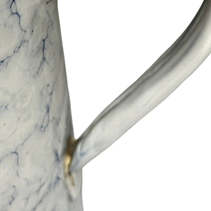 A close-up of a white pot with a marble-like blue veining pattern and a curved handle, isolated on a white background.