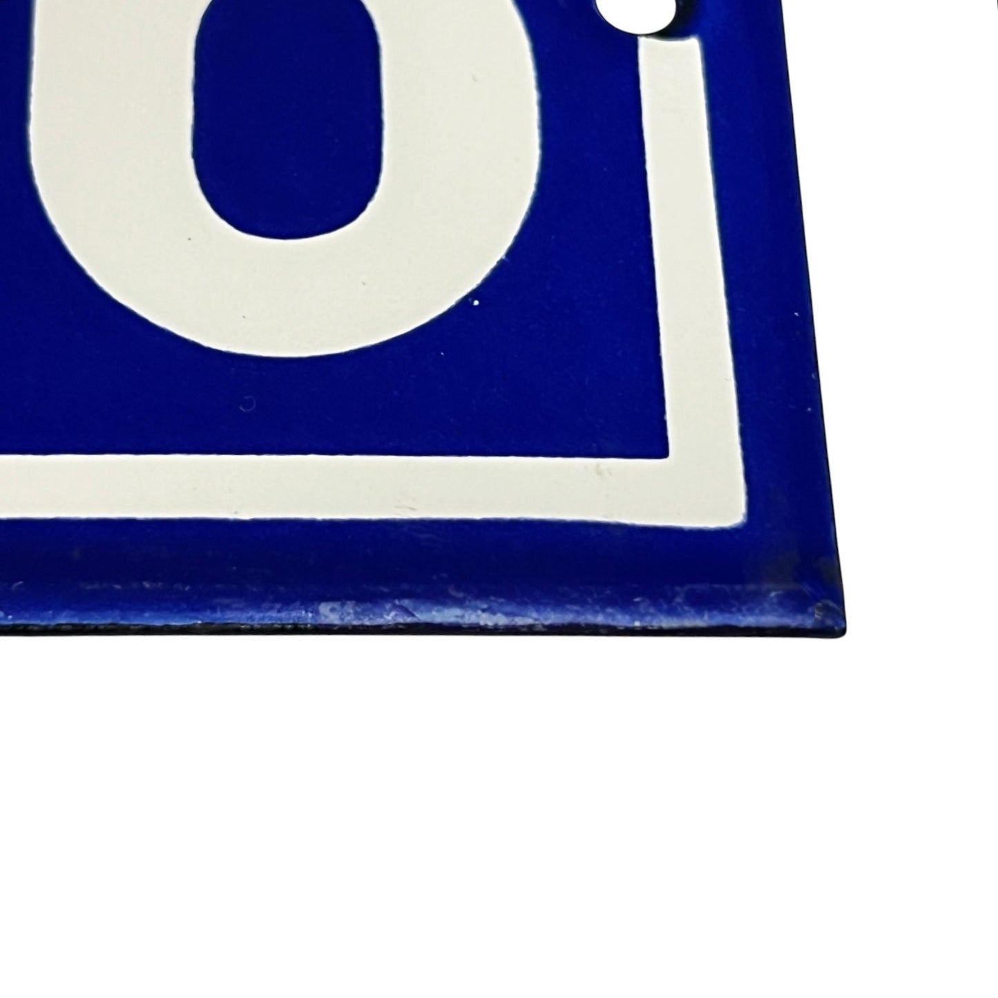 A close-up of a blue and white square sign or tile showing part of a bold white letter and border on a plain white background.