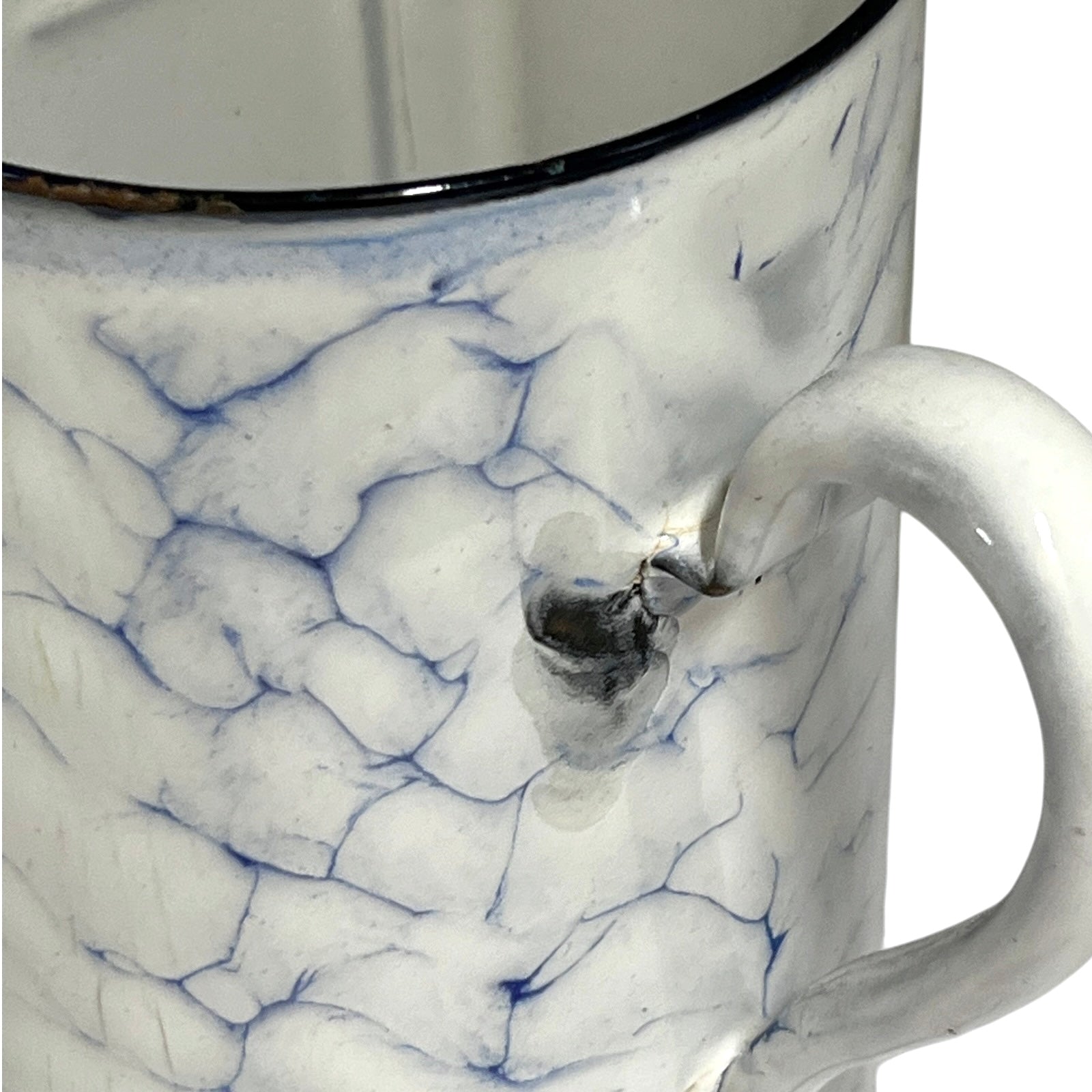 Close-up of a white enamel jugwith a blue crackle glaze pattern and a dark rim, showing a small metallic emblem on the side.