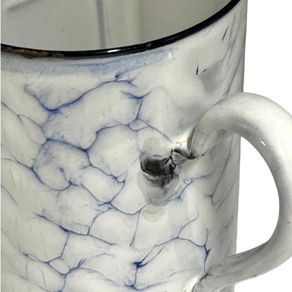 Close-up of a white enamel jugwith a blue crackle glaze pattern and a dark rim, showing a small metallic emblem on the side.