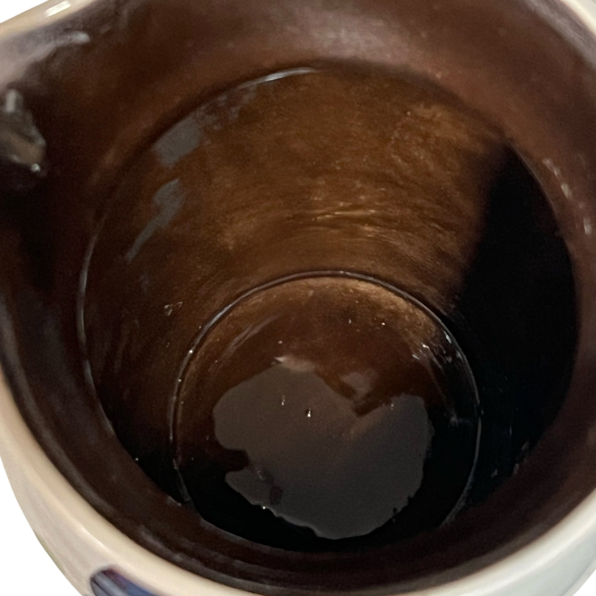 Close-up view inside a dark brown ceramic mug or cup, showing the glossy interior surface and a small amount of liquid at the bottom.