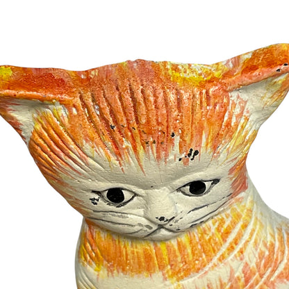 Close-up of a ceramic cat figurine with orange, yellow, and white painted details on a plain white background.