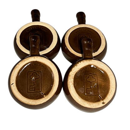 Four brown ceramic escargot plates  shown from the rear on a white background. Each plate  features a handle and a glossy brown glaze with a cream-coloured rim and a key makers stamp for Emile Henry.