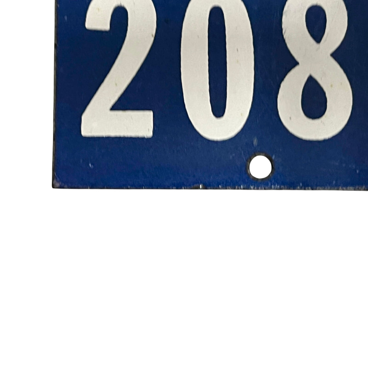 A close-up of a blue rectangular sign or plaque with large white numerals '208' and a small round hole near the bottom right of the numbers, shown against a white background.
