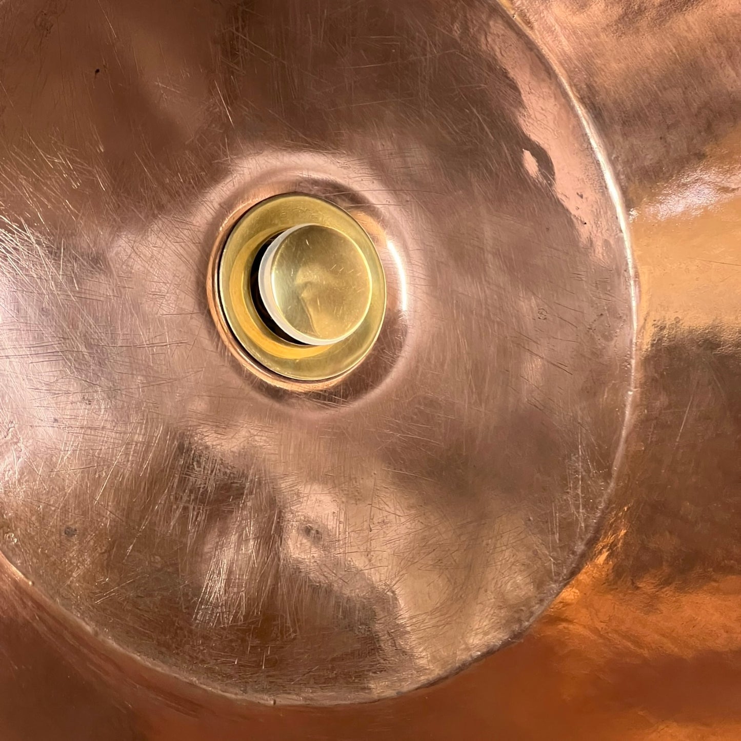 Close-up of a copper sink with a brass drain plug.