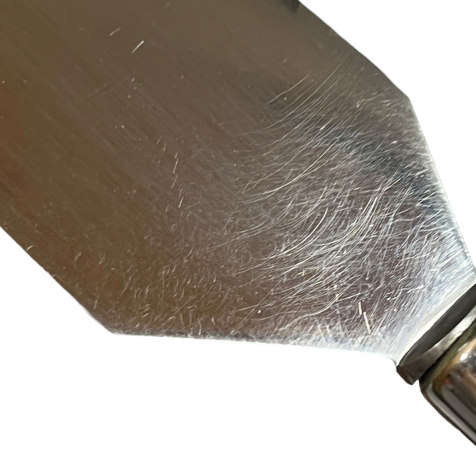 Close-up of a metal spatula blade with visible scratches and a small portion of the metal handle against a white background.