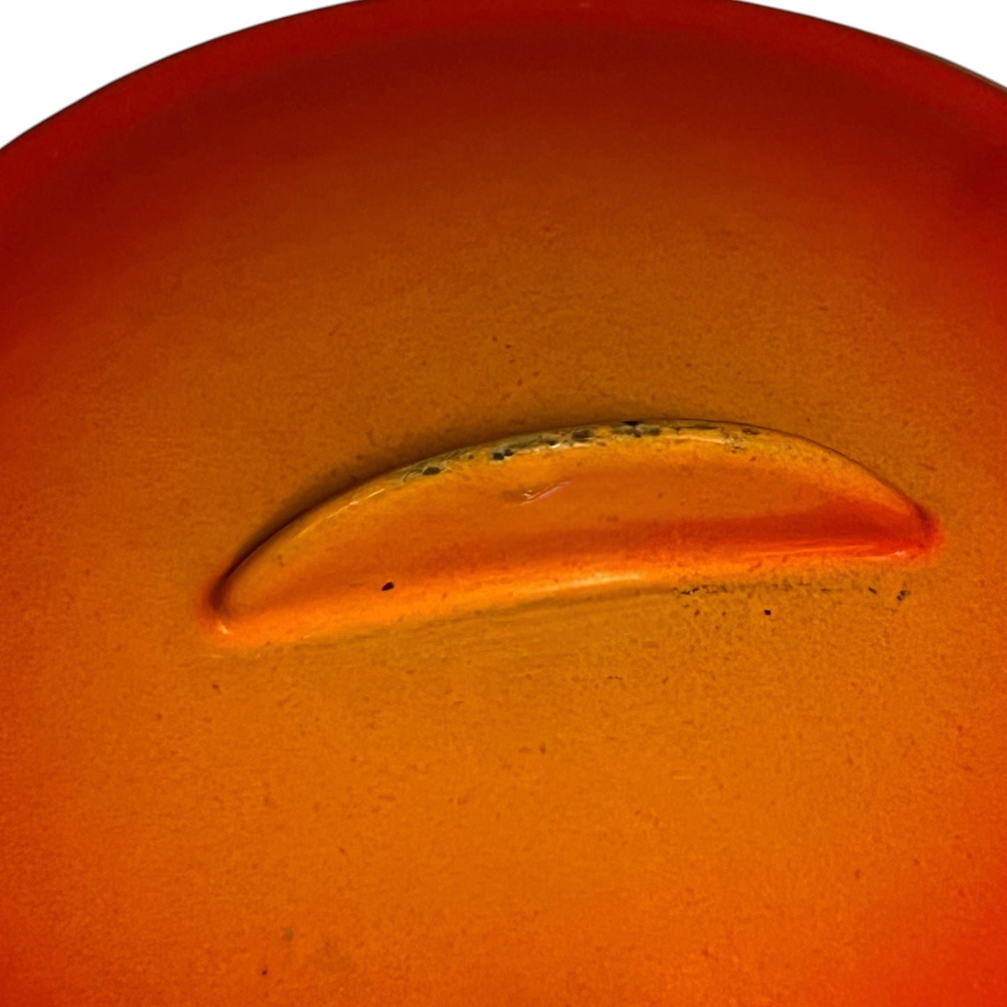 A close-up of a glossy orange-red bean pot, possibly a small accessory or component, set against a matching orange background.