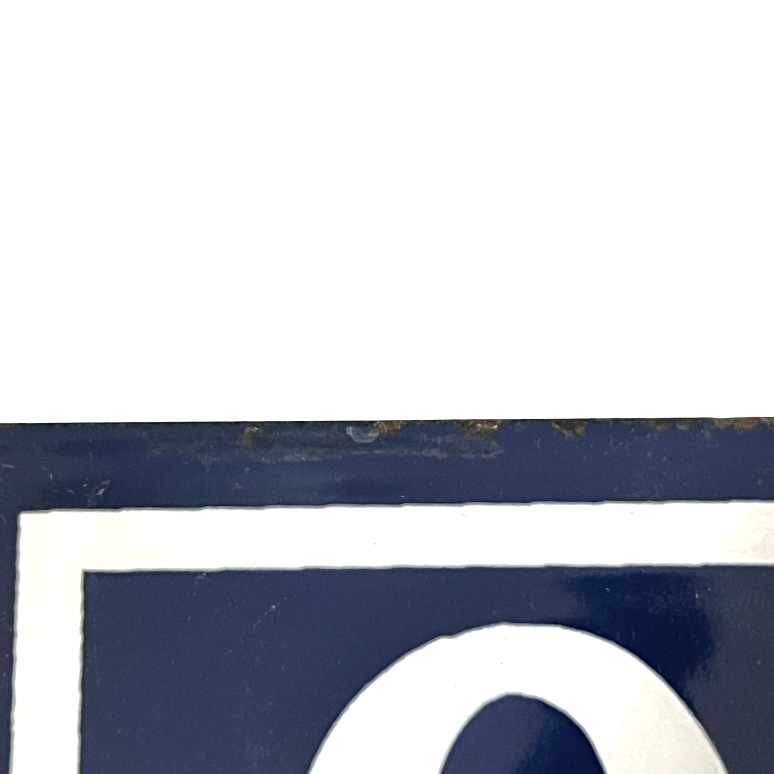 Close-up of a dark navy blue sign or panel with a white border and part of a white numeral visible, against a mostly white background.