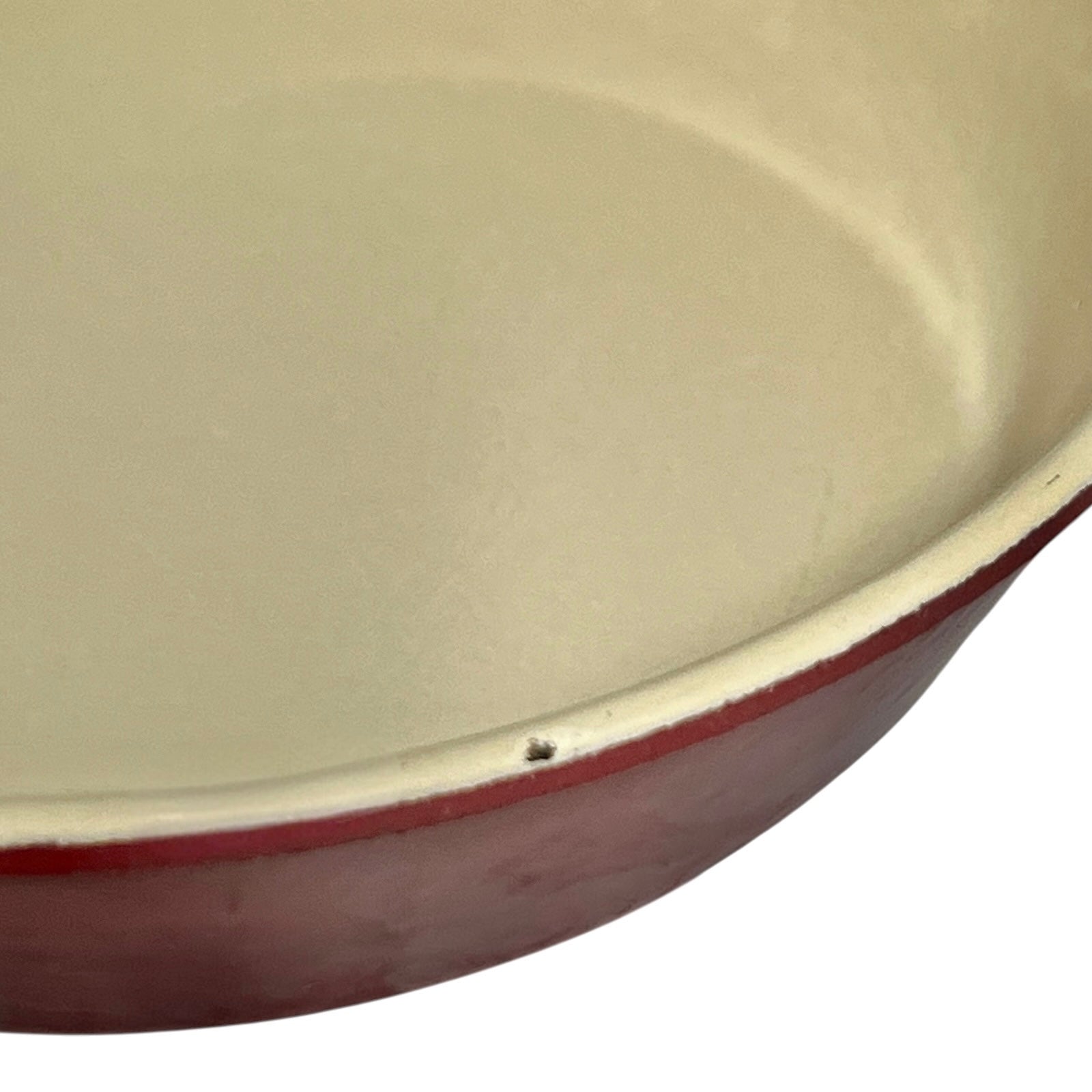 Close-up of a round enameled cast iron skillet showing the cream-colored interior and a dark red exterior rim against a white background.