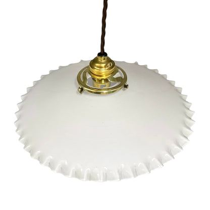 A vintage-style pendant light with a white, scalloped-edge glass shade and a brass metal fixture, suspended by a dark brown cord against a plain white background.