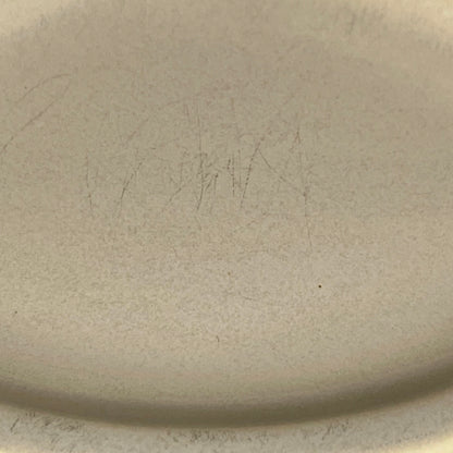 Close-up of a light beige ceramic surface with faint pencil-like markings and a curved rim visible at the bottom edge.