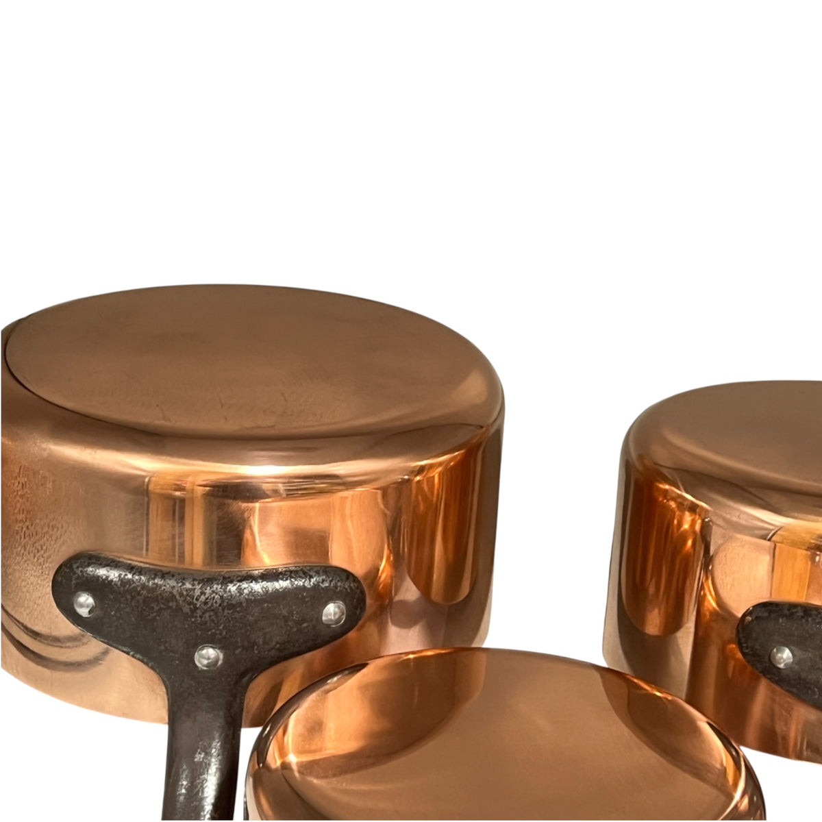 A close-up of a set of copper cookware pots with dark metal handles, shown against a plain white background.