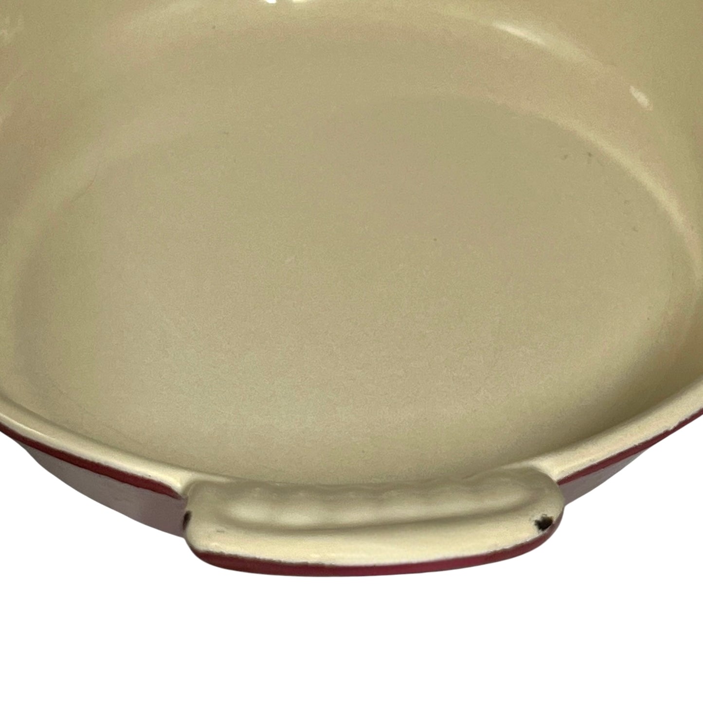 Close-up of a round baking dish or casserole dish with a cream-colored enamel interior and a dark red rim, set against a plain white background.