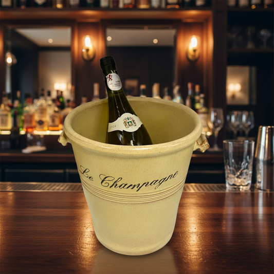 Bottle of champagne in a 'Le Champagne' bucket on a bar counter with a blurred bar background.