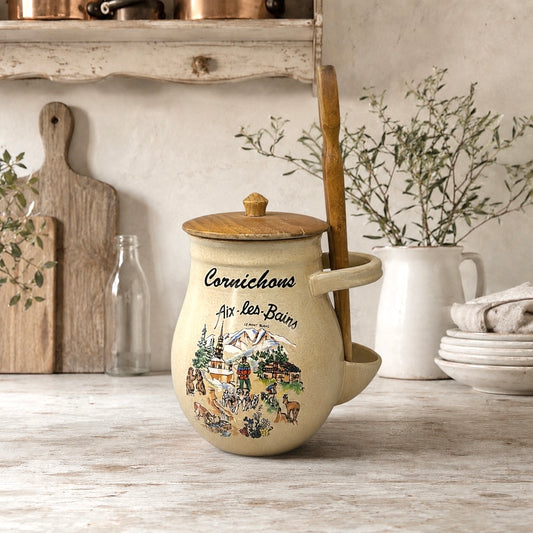 Decorative teapot with a scenic design on a wooden surface, surrounded by kitchen items.