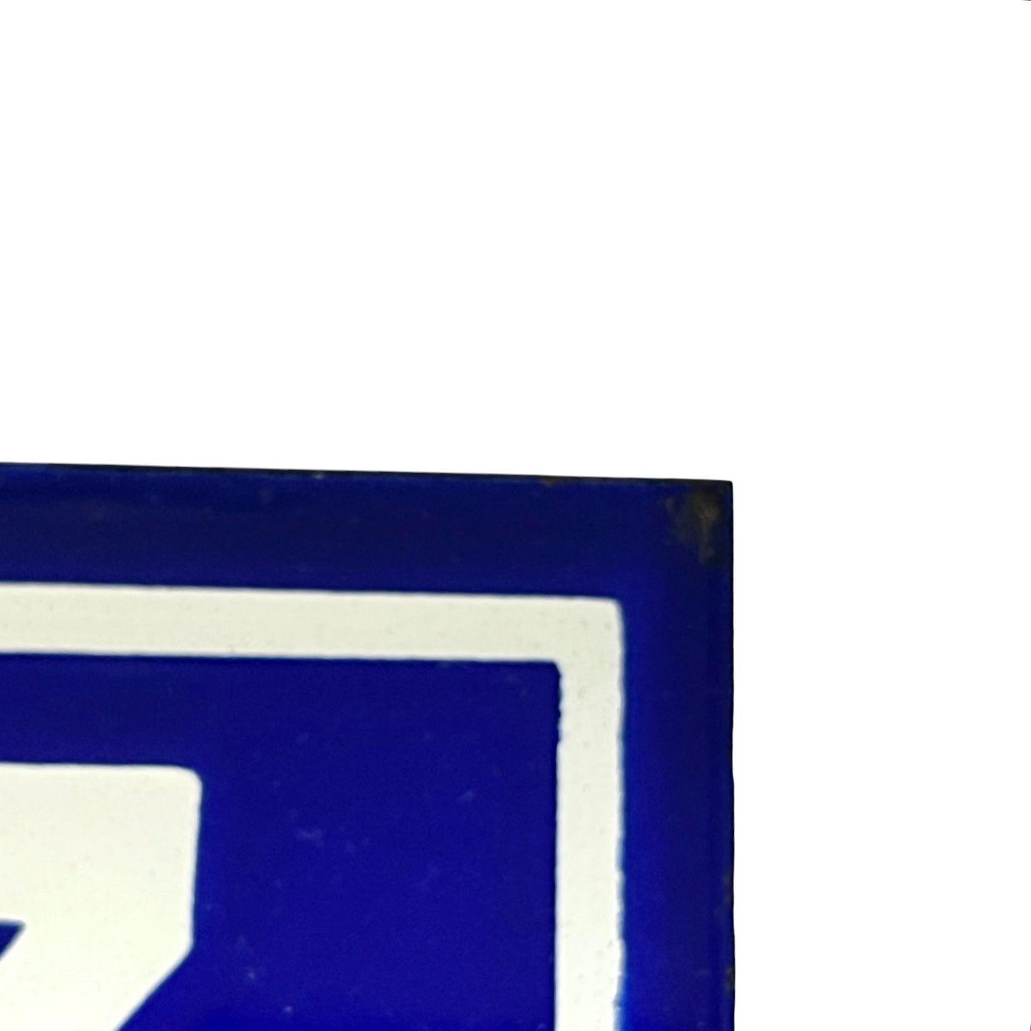 A close-up corner of a blue and white sign or sticker, showing a blue field with a white border and partial white symbol on a white background.