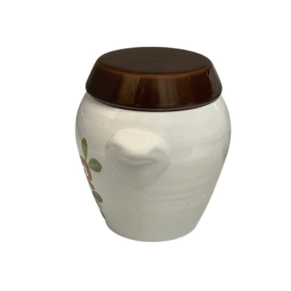 A small ceramic jar with a rounded white body, a brown lid, and a partial floral decoration on the side, shown against a plain white background.
