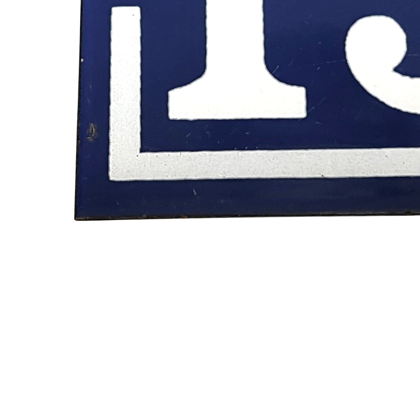 Close-up of a blue and white sign or plaque showing part of a white symbol on a dark blue background, photographed against a white backdrop.