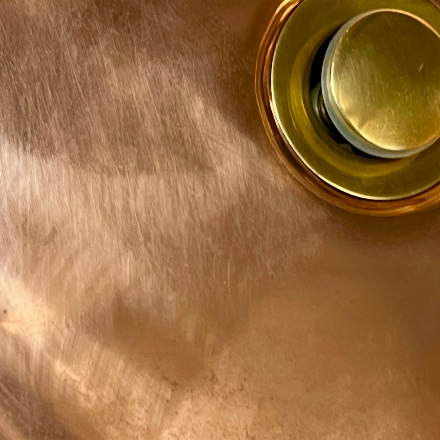 Close-up of a copper sink with a drain plug on a white background