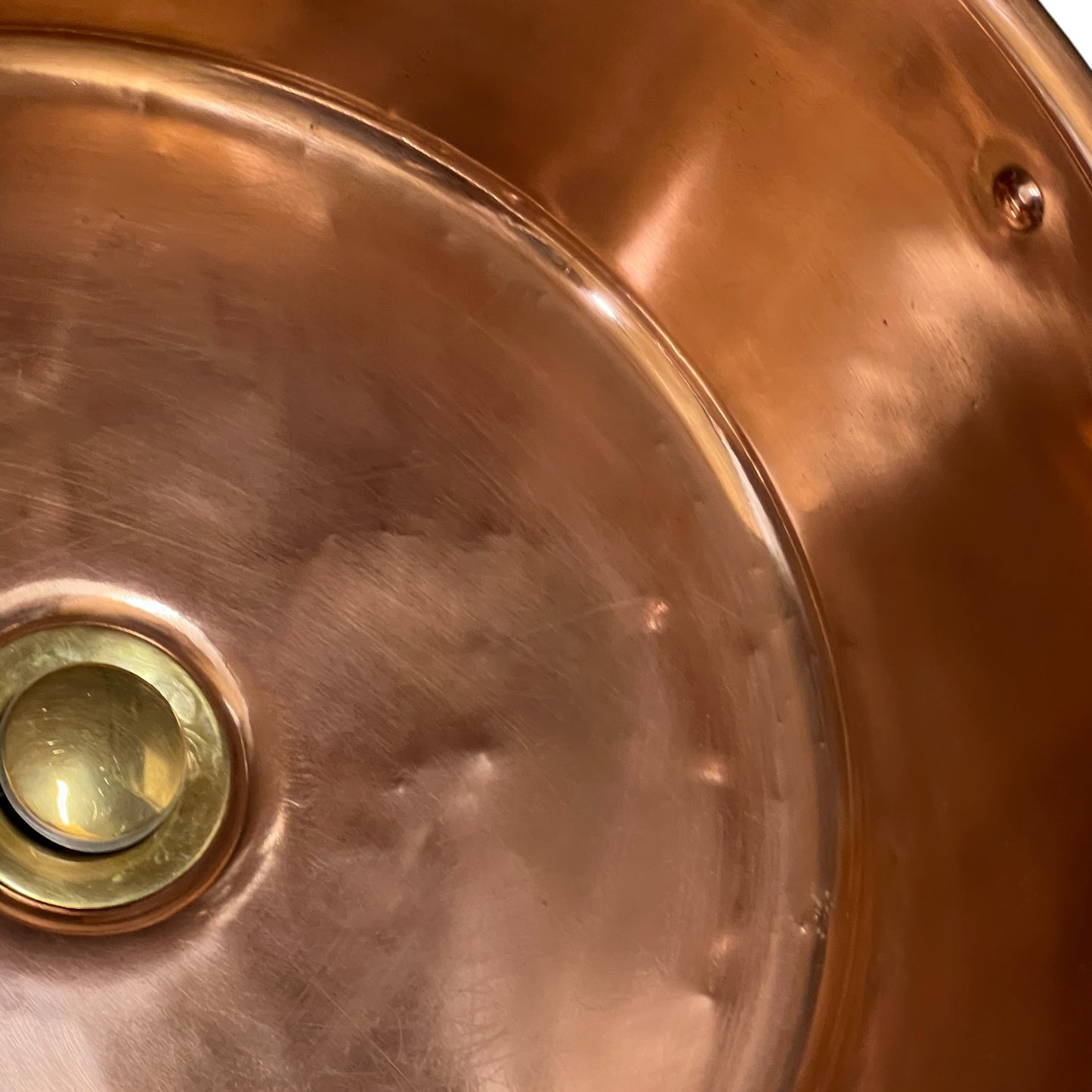 Close-up of the interior bottom of a copper sink with a brass drain.