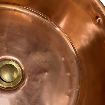 Close-up of the interior bottom of a copper sink with a brass drain.