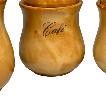 A close-up of a ceramic lidded canister with a warm amber-brown glaze and the word 'Cafe' written in black script on the front, shown against a white background with partial matching canisters at the edges.