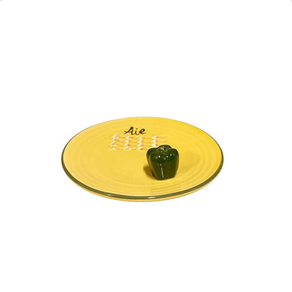 A yellow plate featuring a green pepper and the French word for garlic, “Ail,” designed for grating garlic and perfect for a French farmhouse-style kitchen, set against a white background.